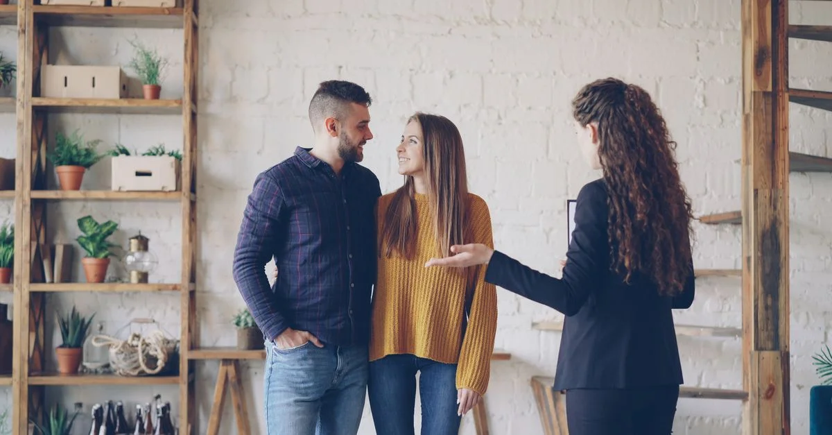 Jeune couple discutant des options immobilières avec un agent dans un appartement en loft élégant.
