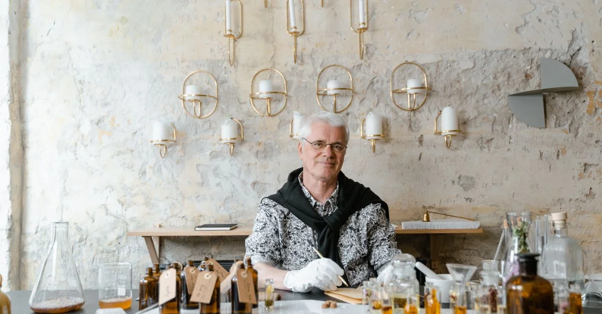 Un parfumeur senior assis parmi des bouteilles de parfum dans un cadre rustique, créant des senteurs uniques.